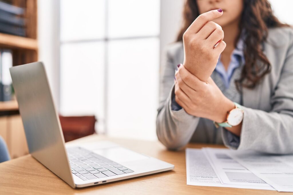 Woman at desk holding her wrist in pain while working on a laptop