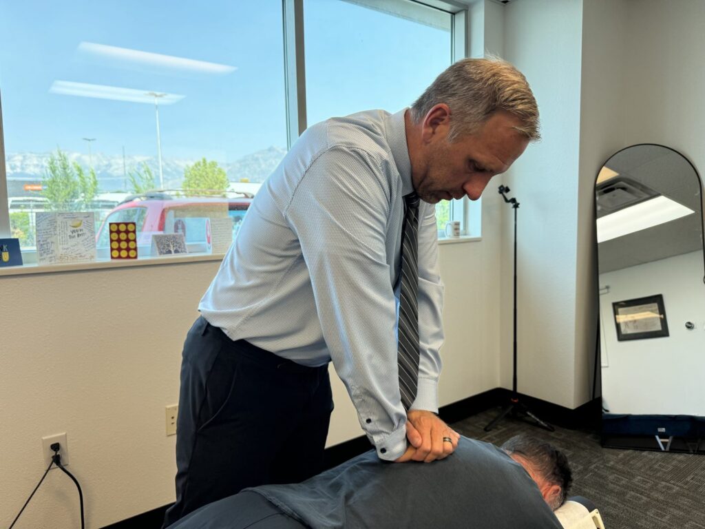 Chiropractor in light blue shirt and tie adjusting patient's lower back in modern office with mountain view