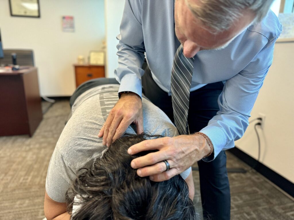 Chiropractor performing hands-on neck and upper back examination on seated patient in clinical setting